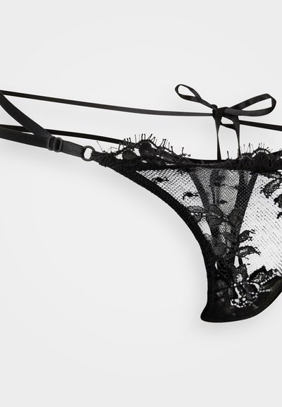 Melna mežģīņu tangas ar smalku ziedu dizainu, tām ir plāni regulējami siksniņas un mīksta tīkliņa tekstūra. Atklāta mugura ar rūpīgi veidotiem malējumiem.