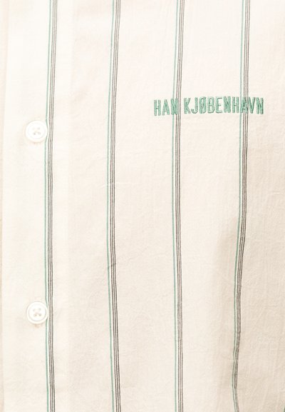 Λευκό πουκάμισο με λεπτές κάθετες πράσινες και μαύρες ρίγες, δύο λευκά κουμπιά και πράσινα κεντημένα γράμματα που αναγράφουν «HAN KJØBENHAVN».