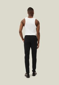 Schwarze eng geschnittene Hose, kombiniert mit einem weißen Tanktop. Glatter Stoff und minimalistisches Design, mit Gesäßtaschen. Aufnahme von hinten.