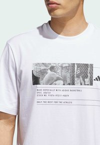 Camiseta de algodón blanca con un estampado gráfico negro y un texto superpuesto relacionado con el baloncesto, con cuello redondo y mangas cortas.