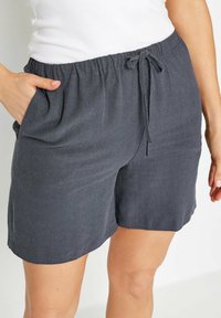 Donkergrijze linnen shorts met een elastische tailleband, aantrekkoorddetail en zijzakken. Zachte textuur en comfortabele pasvorm. De randen zijn glad afgewerkt.