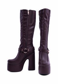 Stivali alti marroni in finta pelle con una piattaforma spessa e un tacco alto a blocco. Presentano una cerniera laterale e una fascia decorativa con una fibbia metallica.