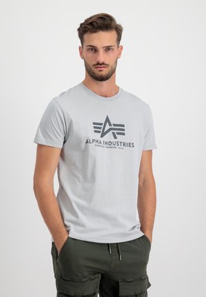 Graues Baumwoll-T-Shirt mit Rundhalsausschnitt, das ein schwarzes "Alpha Industries"-Logo und ein Dreistrich-Design auf der Vorderseite aufweist.