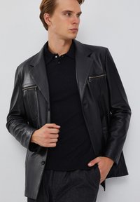 Zwarte leren jas met een op maat gemaakte snit, twee ritszakken op de borst en een gladde textuur. Draag dit over een donker polo shirt.