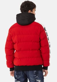 Red padded jacket with a black hood; features a ribbed hem and contrasting white sleeve design. Textured finish with quilted stitching.