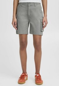 Shorts cargo gris avec fermeture à bouton, poches latérales et coupe droite. Associés à des chaussures de sport oranges, sur un fond neutre.