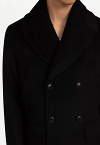 Svart peacoat i ullblandning med bred ribbad krage, dubbelknäppt knäppning och två framfickor. Texturerat tyg, skräddarsydd passform.