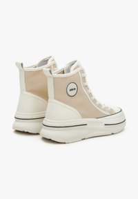 Białe tenisówki w stylu high-top z gładką cholewką, lekko beżowym panelem z tkaniny, okrągłym akcentem logo oraz grubą białą podeszwą z czarnym paskiem.