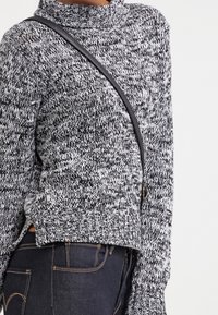 Maglione lavorato a maglia con un alto motivo testurizzato in bianco e nero, con fessure laterali e una vestibilità rilassata. Abbinato a jeans in denim scuri e una borsa a tracolla.