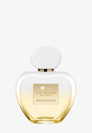 Flacon de parfum en verre transparent avec bouchon blanc arrondi, base dégradée dorée et étiquette dorée indiquant "Her Golden Secret Banderas."