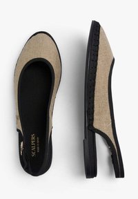 Plátěné slip-on boty s béžovým svrškem, černými detaily a gumovou podrážkou. Obsahují pletený prvek po straně a minimalistický design.