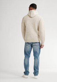 Maglione cappuccio lavorato a maglia di un beige chiaro, con un motivo testurizzato, polsini e orlo a costine, abbinato a jeans azzurri chiari e sneakers bianche.