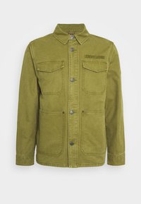 Olivově zelená košilová bunda s límečkem, dvěma náprsními kapsami s klopami, dvěma nižšími kapsami se švy a vyšitým logem "Tommy Jeans" na hrudi.