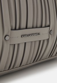 Szara plisowana skórzana torba z metalowymi ćwiekami i centralnie umieszczoną plakietką z logo "KARL LAGERFELD" na przeszytym pasku.
