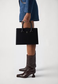 Black leather handbag with structured design, short handles, and gold hardware; paired with knee-high brown leather boots.