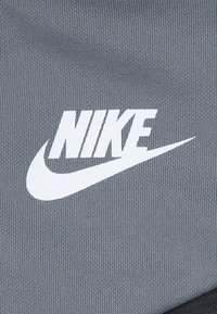 Grauer Stoff mit einer strukturierten Oberfläche zeigt ein auffälliges weißes Nike-Logo und einen Swoosh, zentral auf dem Material platziert.