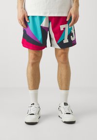 Pantalones cortos deportivos coloridos y estampados con un diseño geométrico en turquesa, rosa y azul marino. Incluyen detalles de malla blanca y una gran impresión de '73'.
