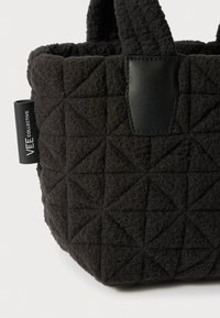 Zwarte gewatteerde stoffen tas met een textuurpatroon van driehoeken, uitgerust met leren accenten en een zijlabel met de opdruk "VEE COLLECTIVE."