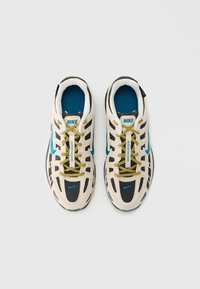 Αθλητικά παπούτσια Nike με εκρού επάνω μέρος, μαύρες και τιρκουάζ λεπτομέρειες, κίτρι�να κορδόνια και πάνελ από υφασμένο πλέγμα με υφή, διαθέτουν σχεδιασμό σόλας με μαξιλάρι.