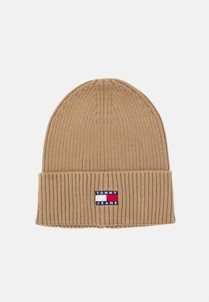 Gorra de punto color marrón con un diseño acanalado y un dobladillo doblado. Presenta un parche con el logo en azul, rojo y blanco en la parte frontal.