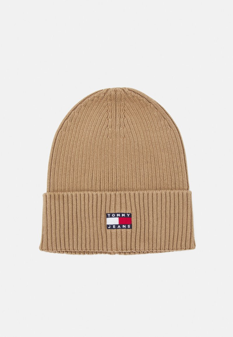 Gorra de punto color marrón con un diseño acanalado y un dobladillo doblado. Presenta un parche con el logo en azul, rojo y blanco en la parte frontal.