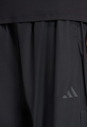 Juoksuhousut mustana, kevyestä kankaasta, jossa on sileä tekstuuri. Housuissa on sivutasku ja sävyyn sovitettu kolme viivaa kuvaava logo.