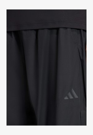 Black athletic shorts made of lightweight fabric with a smooth texture, featuring a side pocket and a tonal three-stripe logo accent.