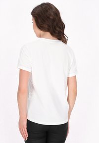 Hvid kortærmet t-shirt med rund halsudskæring og op rullede ærmer, lavet af blødt stof, vist fra ryggen.
