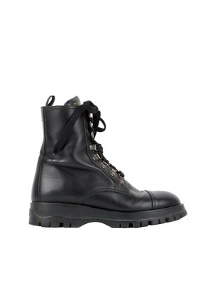 Botte de combat montante en cuir noir avec semelle épaisse en caoutchouc, œillets métalliques, lacets noirs et languette de tirage avec marque, vue latérale sur fond blanc.