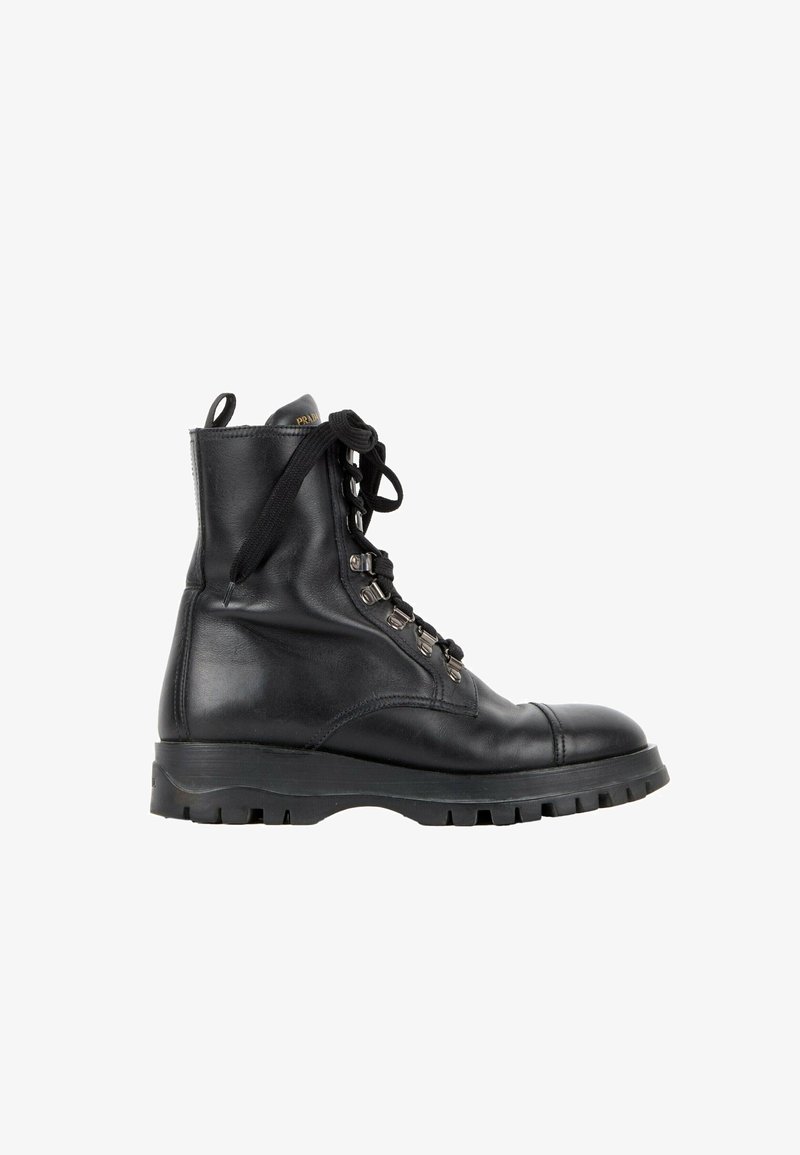 Botte de combat montante en cuir noir avec semelle épaisse en caoutchouc, œillets métalliques, lacets noirs et languette de tirage avec marque, vue latérale sur fond blanc.
