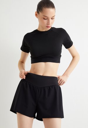 Ensemble de sport noir comprenant un haut court ajusté à manches courtes et un short taille haute. Tissu lisse et extensible avec une coupe décontractée.