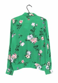 Blusa floreale verde con colletto, maniche lunghe e orlo arricciato, decorata con fiori rosa, bianchi e viola su un tessuto testurizzato.
