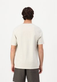 Camiseta de manga corta gris claro hecha de algodón, con un escote redondo y un corte relajado. La vista posterior muestra un diseño sencillo y una textura suave.