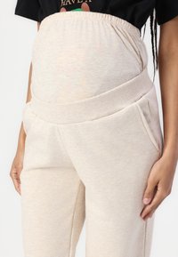 Beige kismama jogger nadrág széles, rugalmas derékkal, oldalsó zsebekkel és puha, texturált felülettel. A kényelem és a könnyű viselhetőség érdekében tervezték.