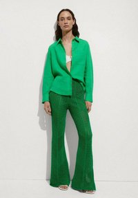 Cămașă verde cu nasturi, dintr-un material ușor, asociată cu pantaloni evazați verzi din croșetat, având un model texturat și un design din tricotaj deschis.