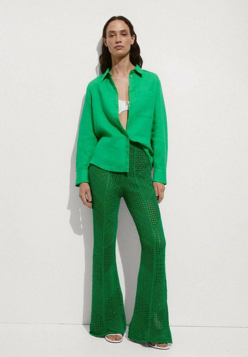 Cămașă verde cu nasturi, dintr-un material ușor, asociată cu pantaloni evazați verzi din croșetat, având un model texturat și un design din tricotaj deschis.