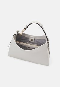 Sac à main en cuir gris structuré avec un dessus arrondi, une poignée accent noir et des accessoires dorés. L'intérieur comprend une poche zippée et plusieurs compartiments.
