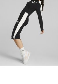 Set atletico nero con strisce laterali bianche, composto da una maglietta a maniche lunghe e pantaloni al ginocchio. Sneakers bianche e calzini alla caviglia completano il look.