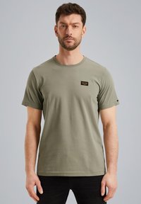 Olive green cotton t-shirt with a round neckline, short sleeves, and a small black label on the upper left side. Smooth texture.