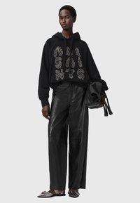 Czarna bluza z kapturem z nadrukiem graficznym, zestawiona z wysokim stanem czarnych skórzanych spodni i metalicznymi balerinami. Minimalistyczny design.