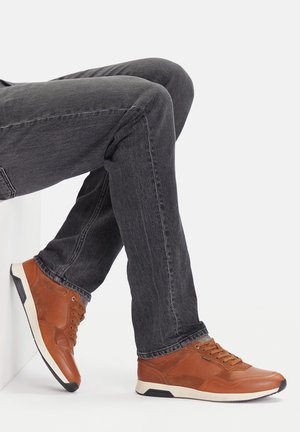 Brązowe sneakersy ze skóry i tkaniny z czarnymi akcentami, o fakturowanej powierzchni, okrągłym nosku i białej gumowej podeszwie. Noszone z ciemnymi dżinsami.