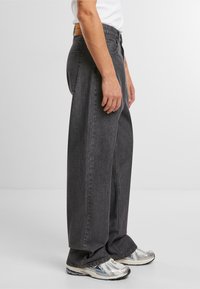 Høyt midje, vide jeans i mørk grå denim, med to sidelommer og en lærlapp bak. Glatt tekstur og løs passform.