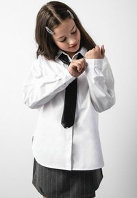 Biała koszula z długim rękawem, z mankietami na guziki i czarnym krawatem; w zestawie z ciemnoszarą spódnicą w prążki. Gładki materiał, staranna konstrukcja.