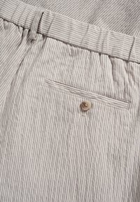 Shorts de tela a rayas en beige y gris claro, con cintura elástica, bolsillo lateral y detalle de bolsillo trasero con botón.