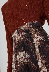 Knitted burgundy sweater with a detailed pattern, paired with a pleated skirt featuring a floral design in black, brown, and cream tones.