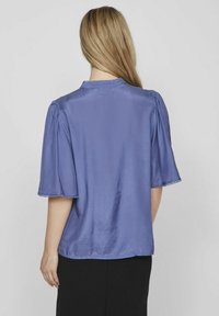 Kortärmad, lila satinblus med rundad halsringning och delikat kant. Slät yta, puffärmar och lös passform.