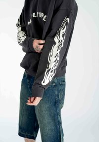 Sort sweatshirt med hvid flammegrafik på ærmerne, med ribbede manchetter, parret med mørke denimshorts. Afslappet, løs pasform.
