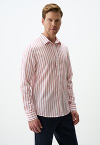 Chemise blanche à manches longues avec de fines rayures rouges, à boutons, col à revers et coupe décontractée, associée à un pantalon sombre.