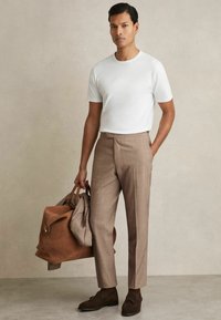 Cămașă albă cu guler rotund, pantaloni bej tailor-iți, pantofi din suede maro și o geantă din piele maro. Design minimalist cu linii curate.