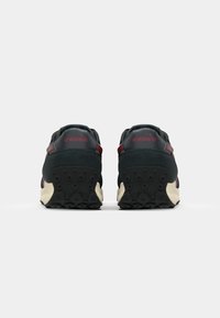 Sneakers with a black upper, maroon accents, and a textured rubber sole featuring circular patterns. Cushioned heel for support.